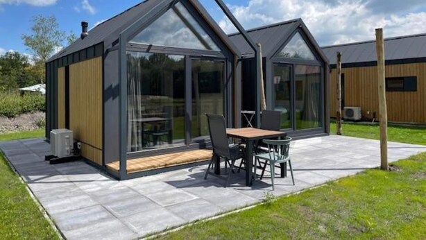 A modern house with a patio, large glass windows, and a wooden deck. - Cozy Holiday Home by the Fishing Pond (Balkbrug)