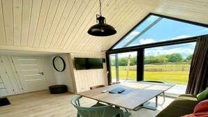 A modern interior with a wooden floor, a dining table with chairs, a sofa, and a large window offering a view of the outdoors. - Cozy Holiday Home by the Fishing Pond (Balkbrug)