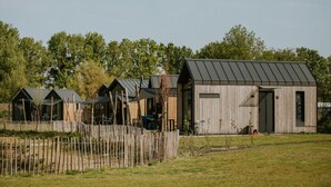 A row of wooden cabins with metal roofs, surrounded by a wooden fence and trees. - Cozy Holiday Home by the Fishing Pond (Balkbrug)