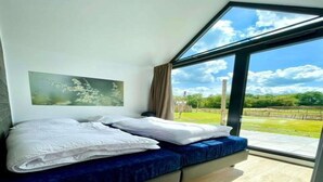 A bedroom with a bed, a painting, and a large window with a view of a green landscape. - Cozy Holiday Home by the Fishing Pond (Balkbrug)
