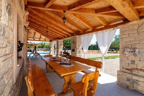An outdoor covered patio with wooden benches and a stone wall. - Rustic Villa With Pool Near Krka Park (Stankovci)