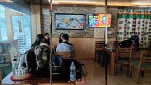 Een restaurantinterieur met houten meubels, een televisiescherm waarop een menu staat en een stenen muur met een inlijsting foto.