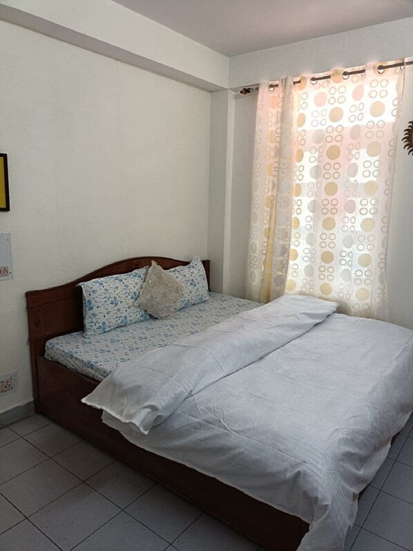 A single-bed room with a wooden headboard, a patterned bedspread, and a white comforter.