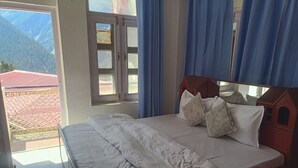 Een slaapkamer met een groot bed, een raam met gordijnen en uitzicht op bergen.