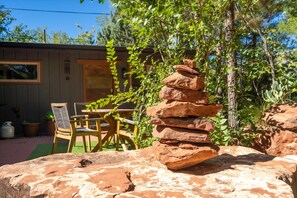 A stack of rocks in a garden area with a wooden chair and table, surrounded by greenery and a building in the background. - Modern Fully Remodeled 3 Bedroom Gem with a Hot Tub and Close to Everything (Sedona)
