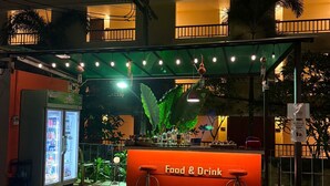 Un espace bar extérieur avec une enseigne indiquant « nourriture et boissons », un réfrigérateur et un auvent vert.
