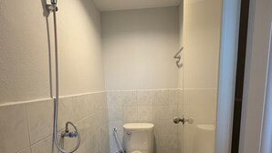 Une petite salle de bain compacte comprenant des toilettes, une douche et un porte-rouleau de papier toilette.