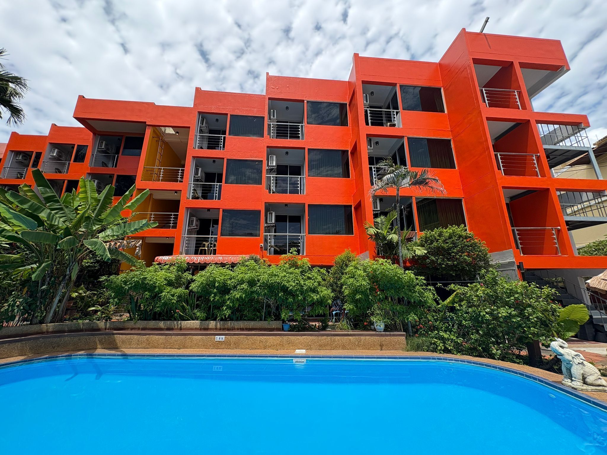 Un immeuble à plusieurs étages doté de balcons, d’une piscine et d’une végétation luxuriante.