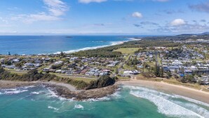 Vue aérienne d’une zone résidentielle côtière, avec des maisons, une plage et un phare.