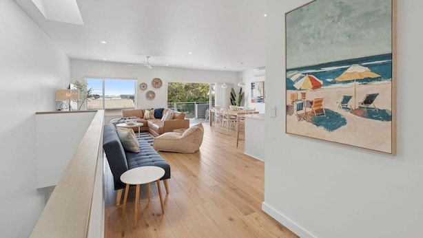 Un grand espace de vie comprenant un long banc, un canapé et une table à manger. Un tableau représentant une scène de plage est accroché au mur.