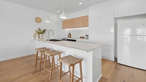 Une cuisine moderne avec des meubles blancs, un îlot central doté de tabourets, un éclairage suspendu et un four encastré.