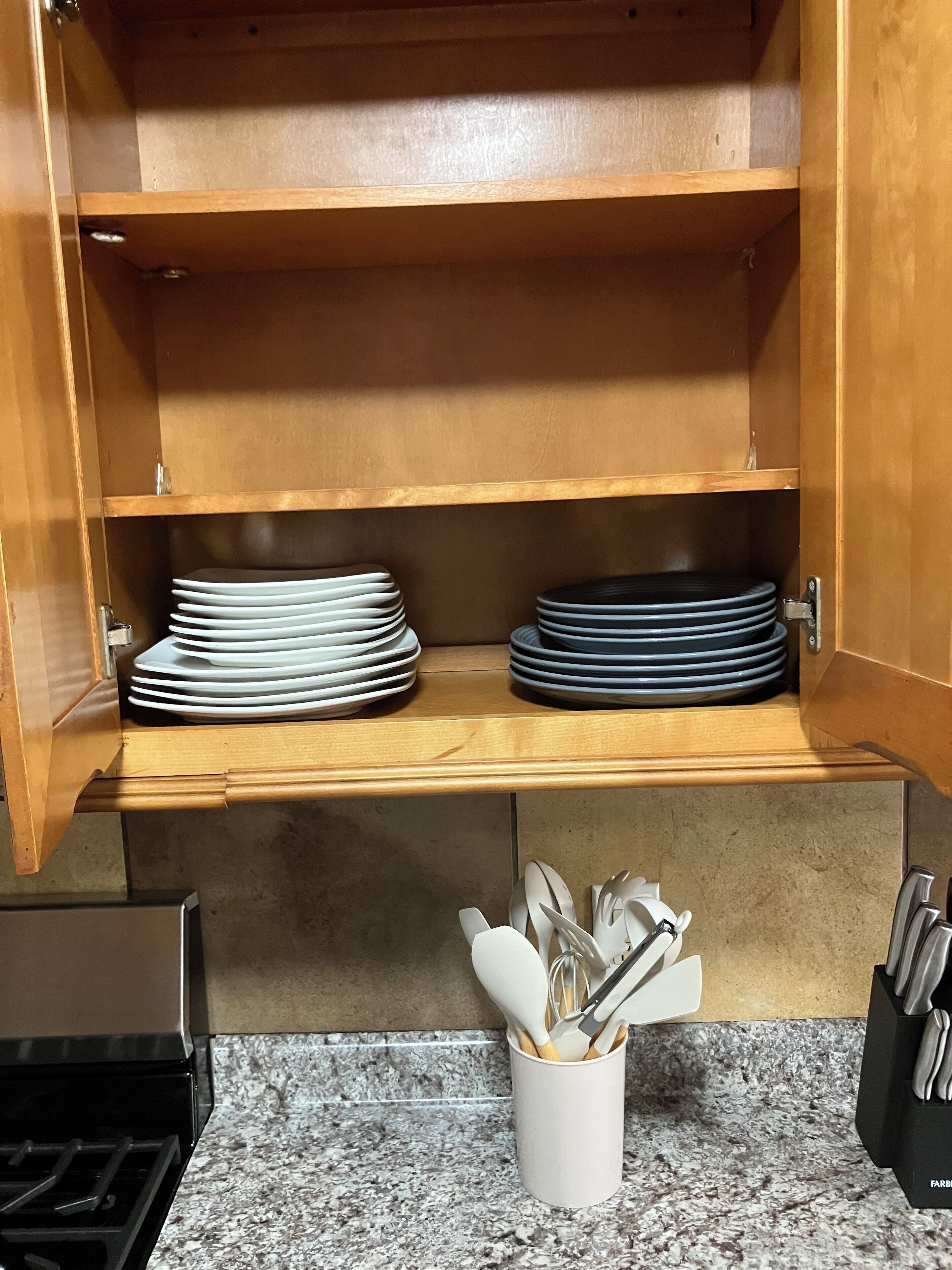 A kitchen with wooden shelves holding stacked plates and a utensil holder on the countertop.