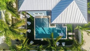 Ein modernes Haus mit Swimmingpool, umgeben von Palmen und Sitzgelegenheiten im Freien.