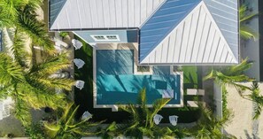 Ein modernes Haus mit Swimmingpool, umgeben von Palmen und Sitzgelegenheiten im Freien.