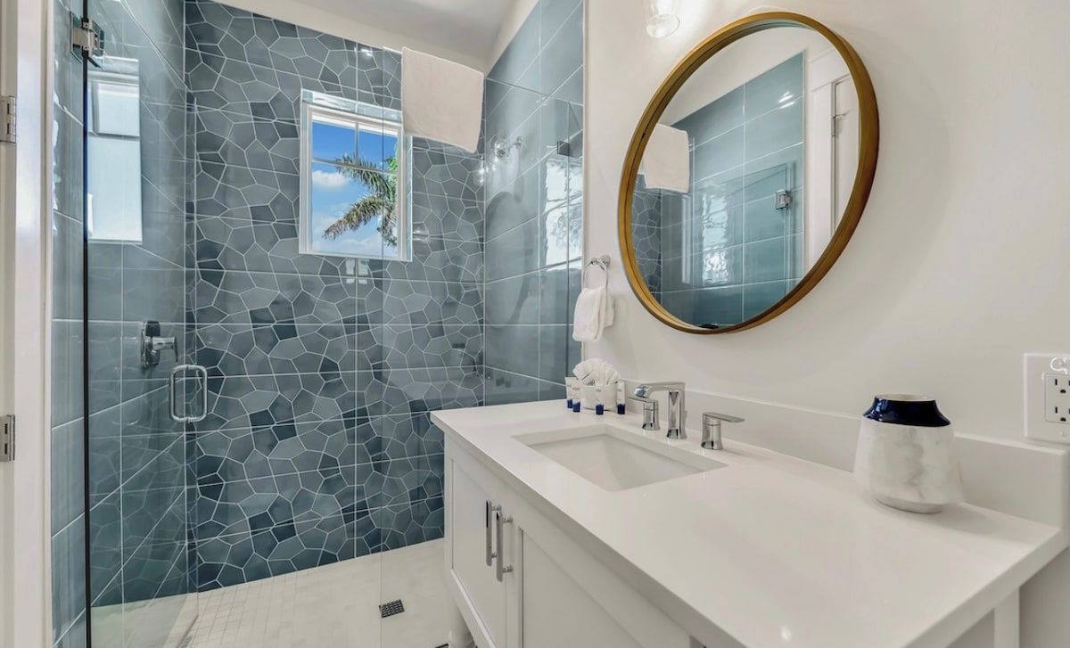 A modern bathroom with a glass shower enclosure, a white vanity with a round mirror, and a tiled backsplash.