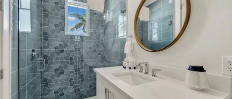 A modern bathroom with a glass shower enclosure, a white vanity with a round mirror, and a tiled backsplash.