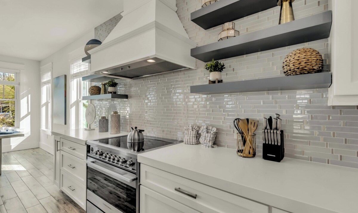 Une cuisine moderne avec des meubles blancs, une cuisinière en acier inoxydable et un dosseret carrelé.