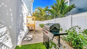 Ein Garten mit Grill, einem Holzstuhl und einem weißen Zaun.