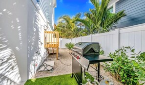 Ein Garten mit Grill, einem Holzstuhl und einem weißen Zaun.