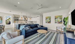 Ein modernes Wohnzimmer mit einem blauen Sofa, einem Couchtisch und einem Essbereich mit einem weißen Tisch und Stühlen.