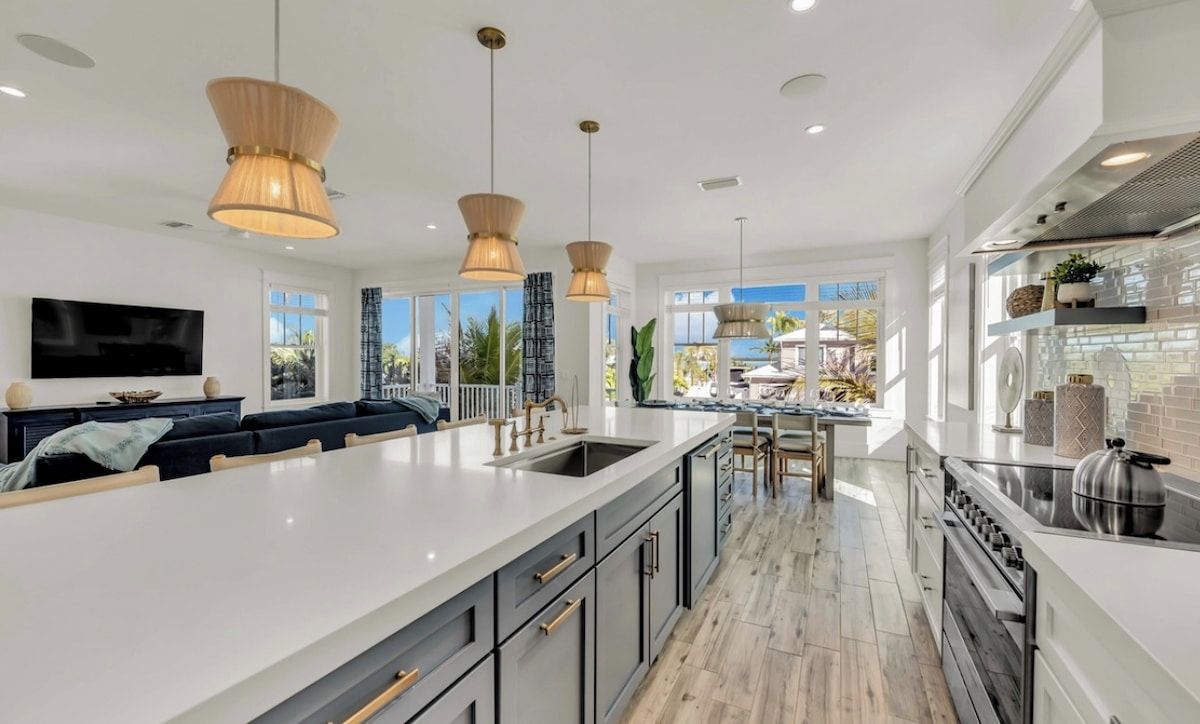 Une cuisine moderne dotée d’un grand îlot central, de luminaires suspendus et offrant une vue sur l’extérieur.