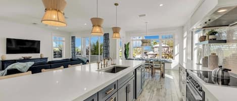 Une cuisine moderne dotée d’un grand îlot central, de luminaires suspendus et offrant une vue sur l’extérieur.
