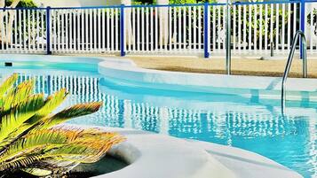 Ein Swimmingpool mit weißem Deck und blauem Zaun.