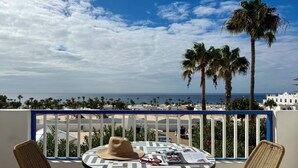 Un balcó amb taula i cadires, amb vista a una platja i palmeres.