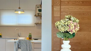 Una cocina moderna con una mesa de madera, un jarrón blanco con flores y una silla color turquesa.
