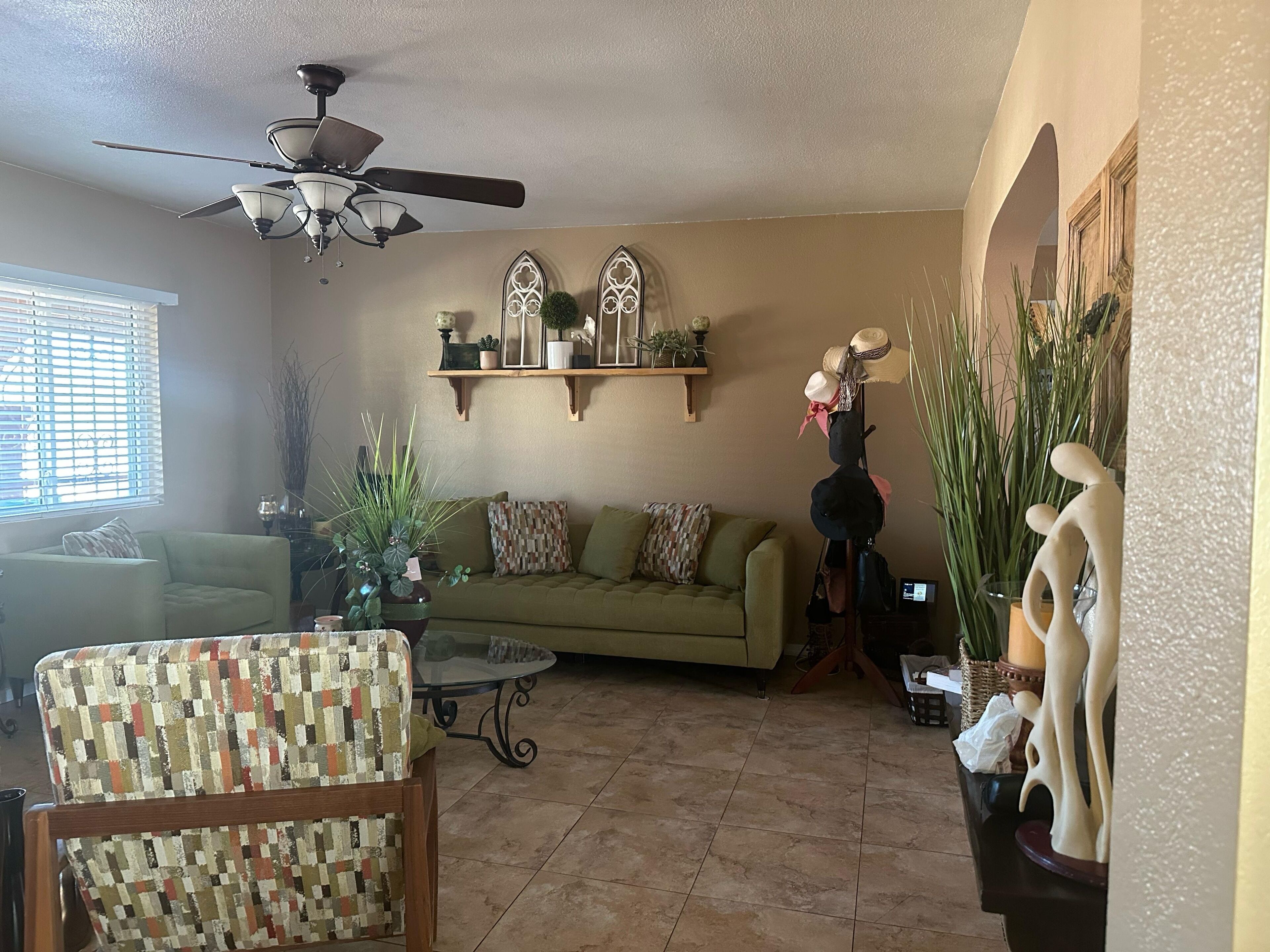 A living room with a ceiling fan, a green sofa, a patterned armchair, and a coffee table.
