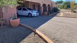 A white car parked in front of a building with a number '1565' on the wall, surrounded by gravel and potted plants. - Enjoyable 2-bedroom house with AC in Green Valley, Nice covered patio. (Green Valley)