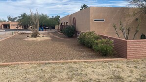 A building with a flat roof and arched windows, surrounded by a landscaped garden with various plants and a gravel pathway. - Enjoyable 2-bedroom house with AC in Green Valley, Nice covered patio. (Green Valley)