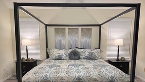 Un letto a baldacchino con tenda, una coperta a motivi e cuscini coordinati, affiancato da comodini con lampade.