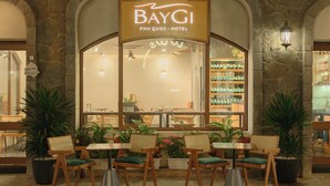 A hotel entrance with a sign reading 'BayGI PHU QUOC - HOTEL,' outdoor seating with chairs and tables, and a view of the interior through the glass. - BayGi Phu Quoc Hotel (Phu Quoc)