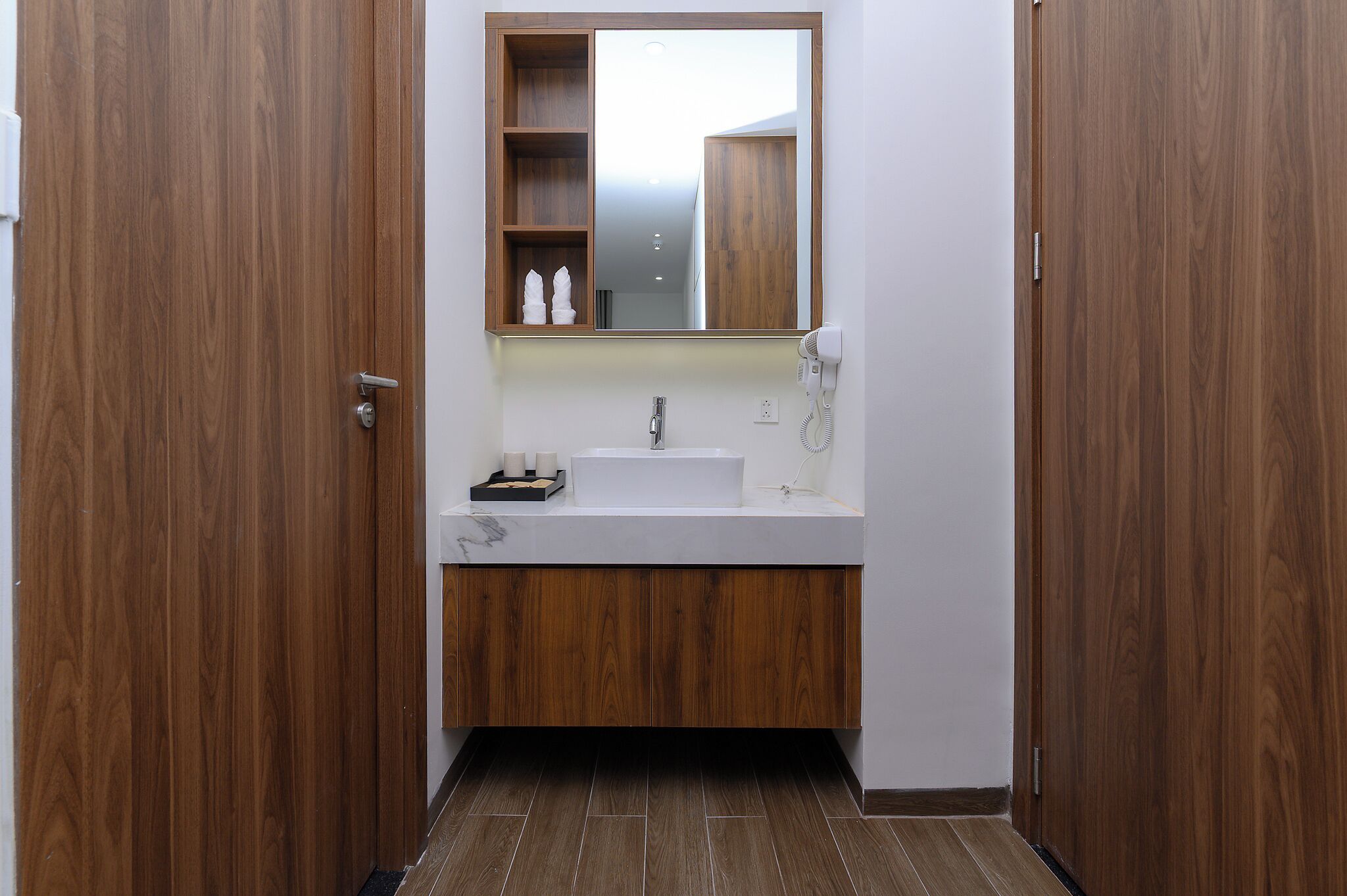 Ein Badezimmer mit einem Holzkosmetikschrank, einem weißen Waschbecken und einem Spiegel darüber.
