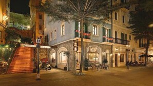 A nighttime street scene with a restaurant named "BayGi" featuring outdoor seating, a staircase leading to an upper level, and a tree in the foreground. - BayGi Phu Quoc Hotel (Phu Quoc)