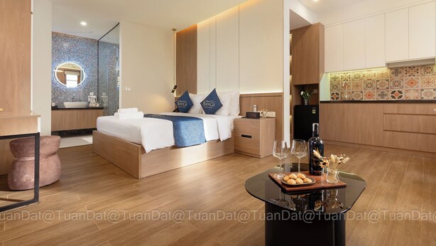 A modern hotel room with a bed, bedside table, and a dining area with a table set for two. - BayGi Phu Quoc Hotel (Phu Quoc)