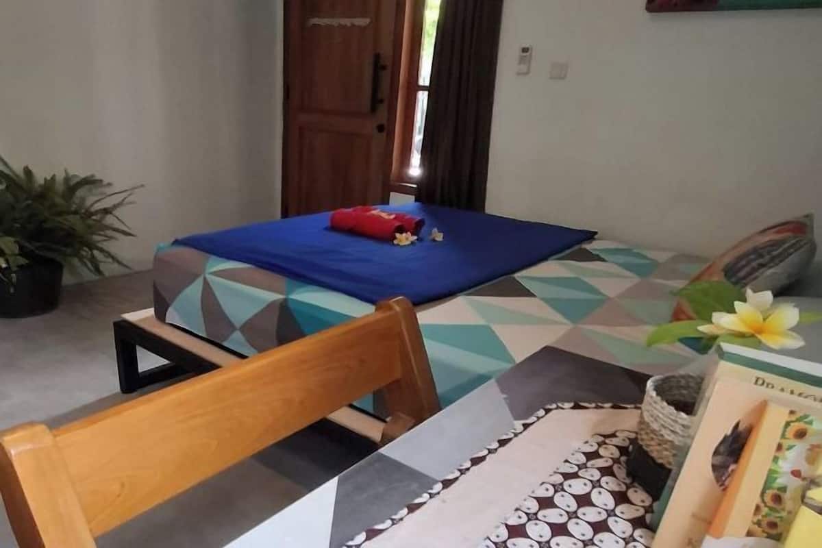 A room with a bed, a chair, a potted plant, and a book on the table.