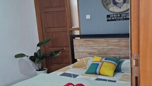 A neatly made bed with a rolled towel and flowers, a wooden headboard, a potted plant, and a wall with a motivational poster. - Bring in House Yogyakarta (Mantrijeron)