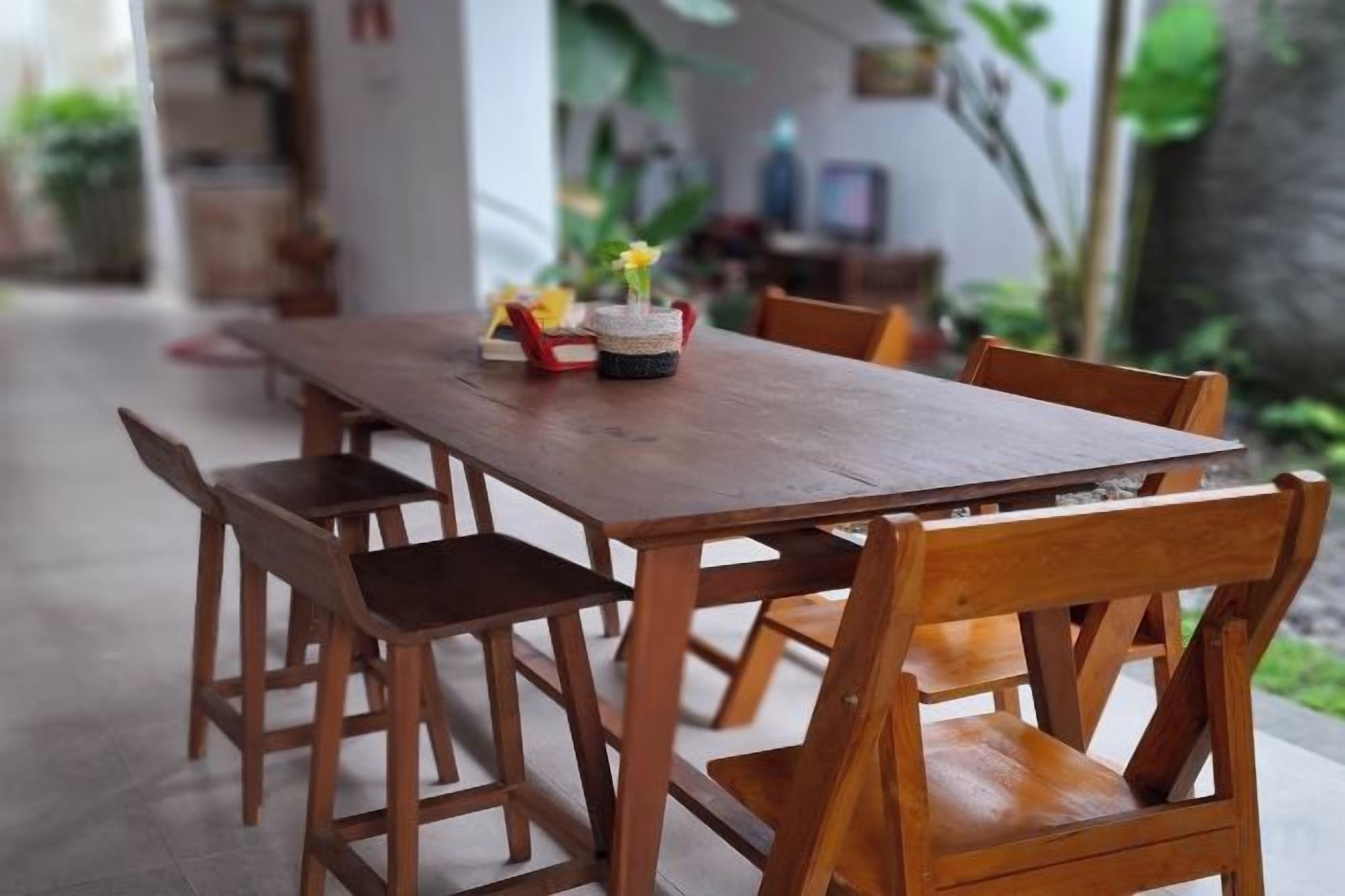 Une table à manger en bois avec des chaises, un panier tressé rempli de fleurs et un téléviseur en arrière-plan.