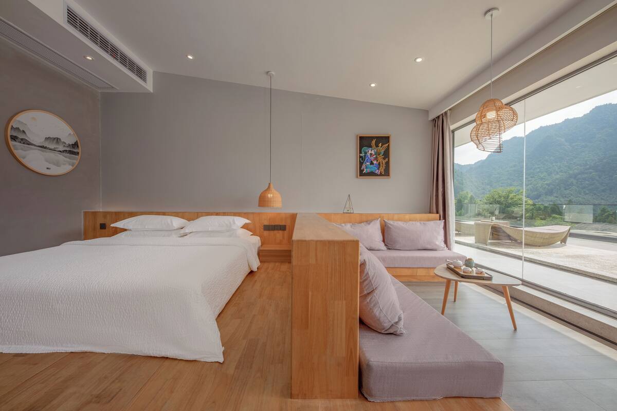 Ein modernes Schlafzimmer mit einem Holzbett, einem Sofa und Blick auf Berge durch große Fenster.