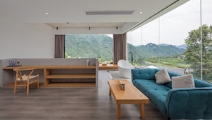 Een moderne woonkamer met een houten bureau, een turquoise bank en uitzicht op bergen door grote ramen.
