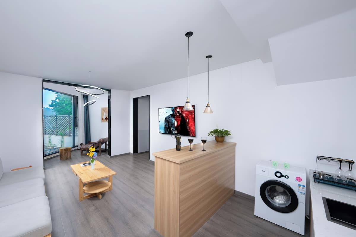 Ein modernes Wohnzimmer mit einer Couch, einem Holztisch, einem an der Wand befestigten Fernseher und einer Waschmaschine in der Ecke.
