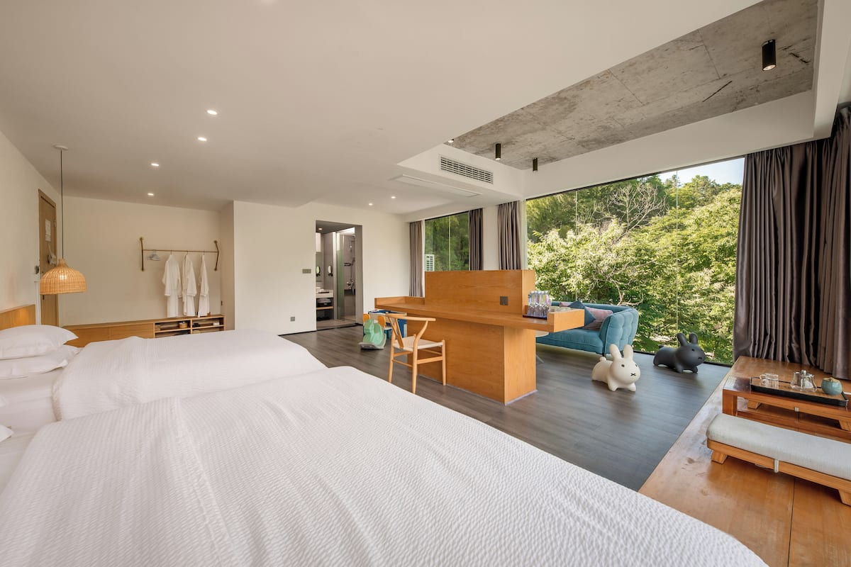 Ein modernes Hotelzimmer mit einem großen Bett, einem Holztisch, einer Couch und Blick ins Freie.