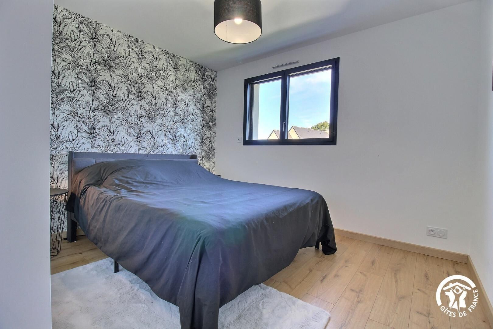 Ein Schlafzimmer mit einem Bett, einem Fenster und einer Wand mit tropischem Wandpapier.