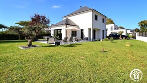 Ein modernes, zweistöckiges Haus mit Terrasse, Gartenmöbeln und einem gepflegten Rasen.