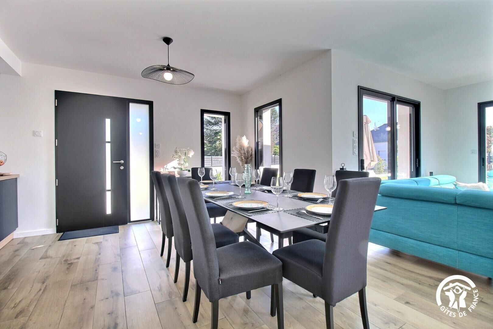 A modern dining area with a dark wooden table set for six, surrounded by grey upholstered chairs.