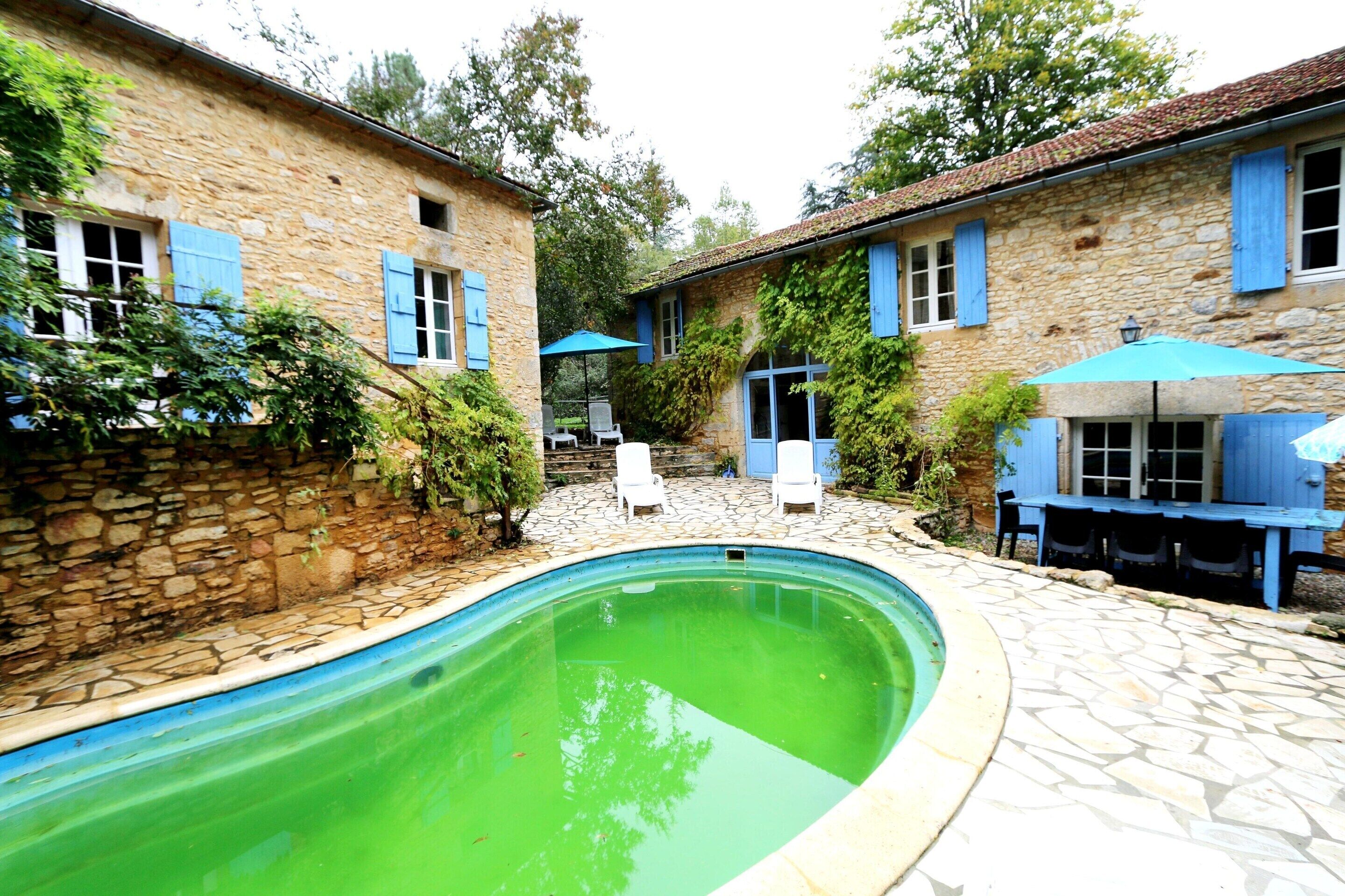 Ein Steinhaus mit Schwimmbad, Außenbereich und blauen Fensterläden.
