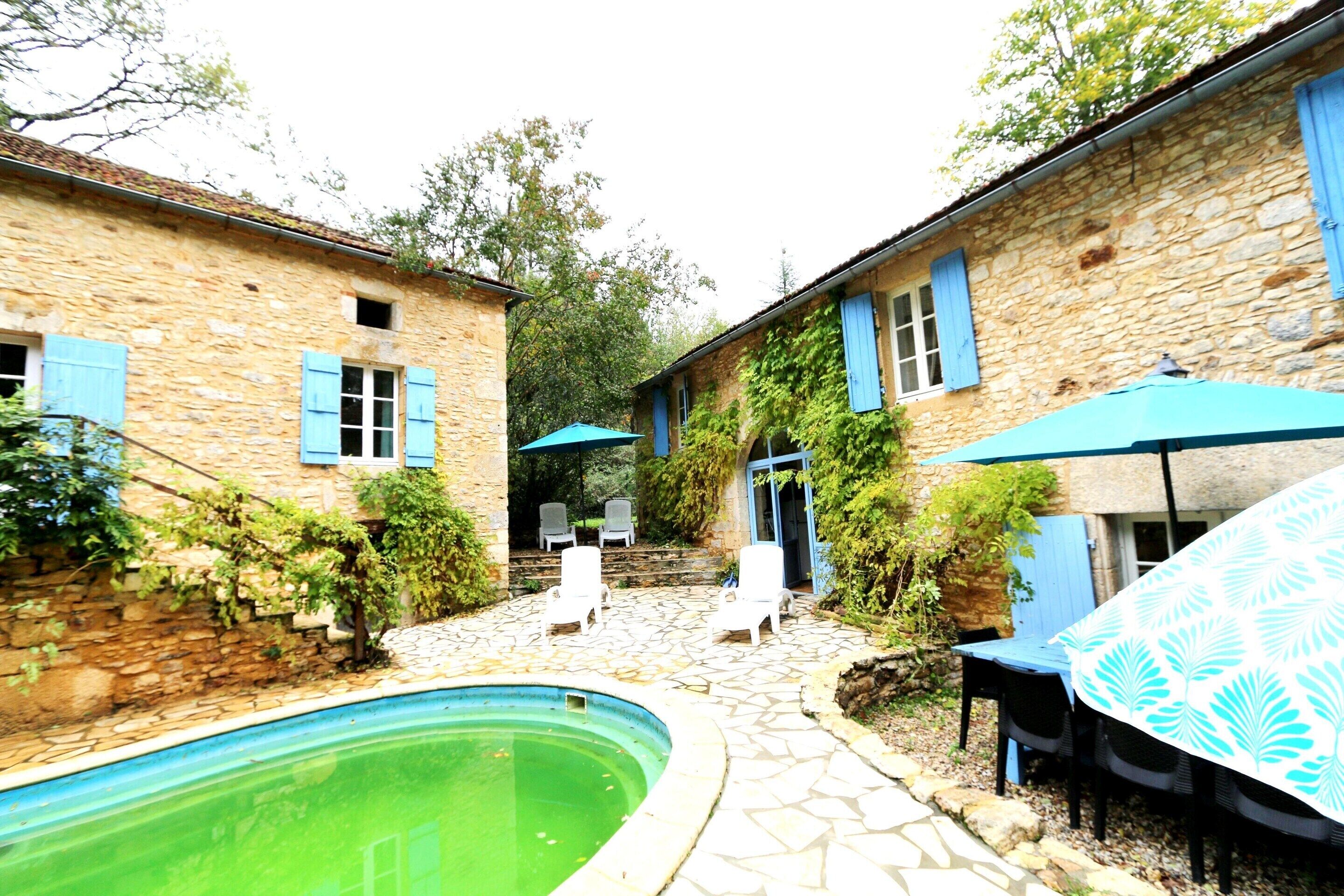 A stone courtyard with a swimming pool, outdoor seating, and a covered table area.