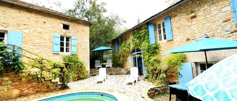 A stone courtyard with a swimming pool, outdoor seating, and a covered table area.